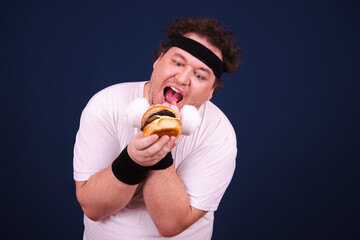 Funny fat man eating burger and doing fitness in the gym.