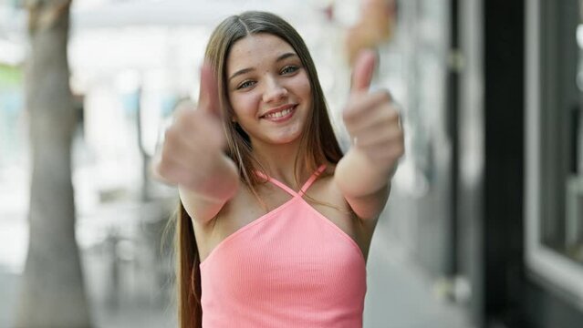 Young beautiful girl smiling confident doing ok sign with thumbs up at street