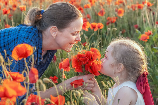 Little girl and her mother with a bouquet of poppies in a field on a summer day