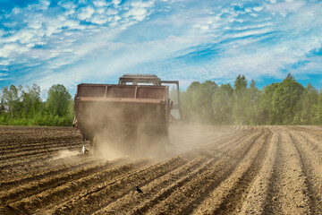 Fototapeta premium Potato planter in agricultural field raises cloud of dust in dry spring during sowing field work.