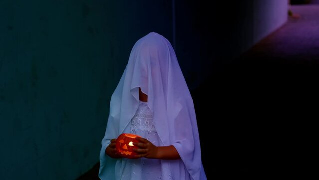 ghost girl 3 years old in white hoodie holds pumpkin candle in hands in creepy house, sad child ghost night, halloween festival concept, frightening mystical events, friday 13th, horror movie scene