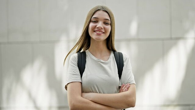 Young beautiful girl student wearing backpack standing with arms crossed gesture smiling over isolated white background