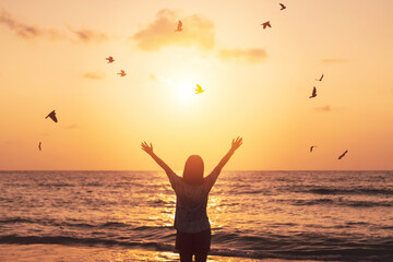 Copy space of woman raise hand up on sunset sky at beach and island with birds flying background. Freedom and travel adventure concept. Vintage tone filter color style.