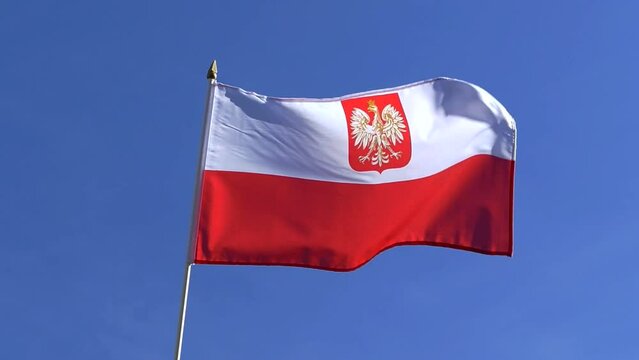 The Polish flag with eagle waving in the wind in the blue sky