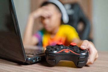 Asian boy sitting with his eyes closed while playing computer games online with game controller...