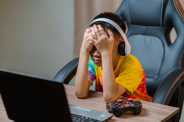 Asian boy sitting with his eyes closed while playing computer games online with game controller...