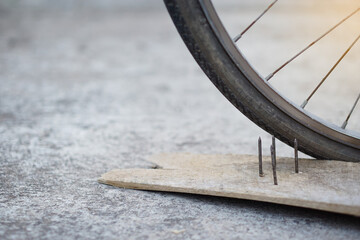Close up nails on wood board and flat bicycle tire. Concept, unsafe , damage. Be careful and look around during cycling on the floor or risk places. Accident can be happened.            - obrazy, fototapety, plakaty