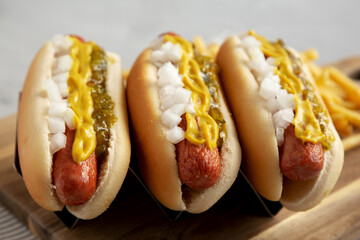 Homemade Deep Fried Hot Dogs with Mustard, Onion and Pickle Relish on a wooden board, side view.