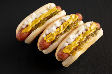 Homemade Deep Fried Hot Dogs with Mustard, Onion and Pickle Relish on a wooden board on a black background, side view.
