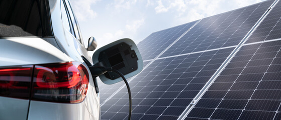 Close up of electric car with a connected charging cable on the background of solar panels.