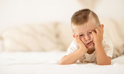 Unhappy tired little boy lying on bed and grimacing