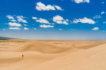 Fototapeta na wymiar Man walking alone in a bright sandy desert landscape during the day