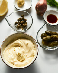 Classic Tartar Sauce ingredients on white marble background. Mayonnaise with dill and capers plus lemon, shallot onion. Worcester sauce and Dijon Mustard. 