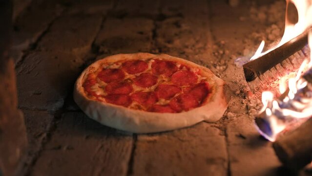Italian pizza pepperoni is cooked in a wood-fired oven. Pizza with salami in hot oven close up. Food video. UHD 4k video. Slight dolly move