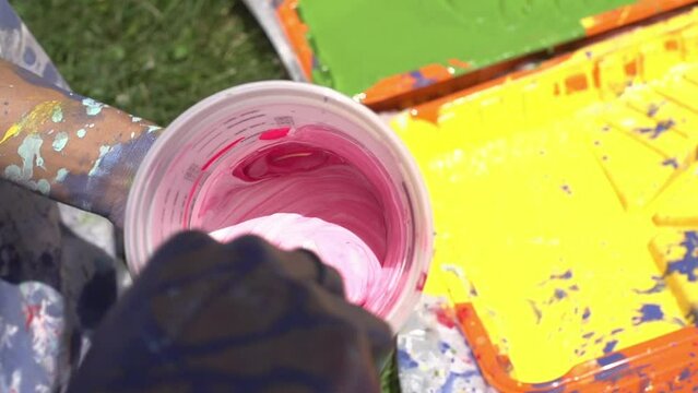 Slow-motion Footage Of A Painted Hand Of A Person Mixing Two Colors Of Paint In A Plastic Container