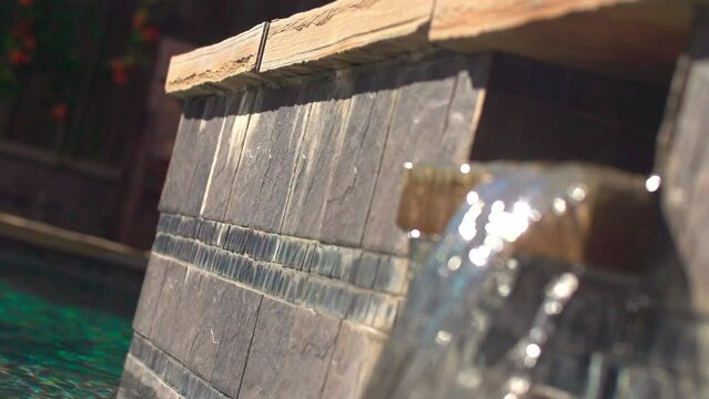 Selective focus slow-motion of a pool wall with a blurred foreground of a small scupper waterfall