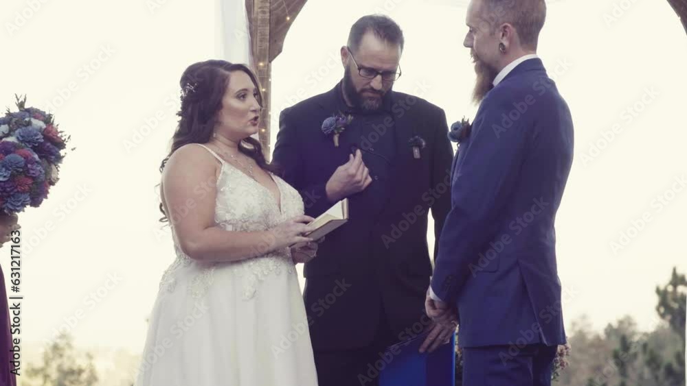 Wall mural marriage officiant reading vows between a caucasian grom and a bride outdoors