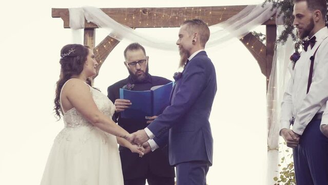 Happy marriage officiant reading wedding vows between a Caucasian grom and a bride outdoors