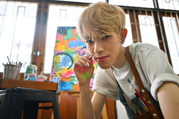 Portrait image of a Young Asian gay Artist boy with colored hair posing with a paintbrush.