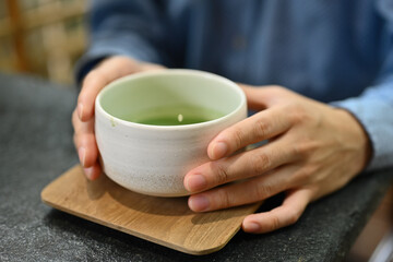 Close up and cropped image of man's hands holding tea cup , Japanese traditional matcha tea,...