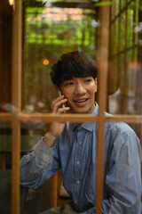 Portrait shot through window, Young Asian man talking on the phone while sitting in Japanese style restaurant.