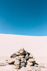 Fototapeta na wymiar Vertical shot of a pile of stones and dunes of Saujil under the clear sky in Catamarca, Argentina.