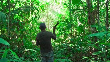 Slow motion of an old man with a sword walking in the dense green jungle