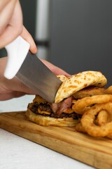 Freshly-prepared cheeseburger with fried onion rings served on a wooden cutting board.