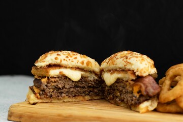 Freshly-prepared cheeseburger with fried onion rings served on a wooden cutting board.