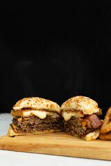 Freshly-prepared cheeseburger with fried onion rings served on a wooden cutting board.