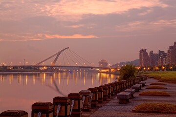 Sunset scenery at a riverside park in Taipei City Taiwan, with the beautiful cable-stayed Dazhi Bridge over Keelung River, the majestic Grand Hotel in background & residential towers on the waterfront
