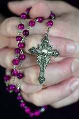 Close up of an woman with prayer hands folded to the chest holding a Rosary beads. Building deeper relationship with through praying The Rosary everyday concept.