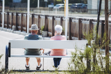 Couple de personnes âgées de dos assises sur un banc 