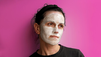  brunette, with applied cream on her face, with a thoughtful look. on a pink background 