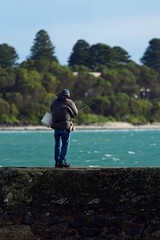 Mature man in casual attire standing on a stone wall fishing
