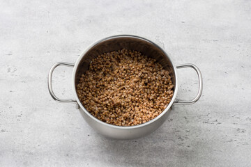 Boiled buckwheat in a saucepan on a gray textured background, top view. Cooking a delicious vegan meal or breakfast