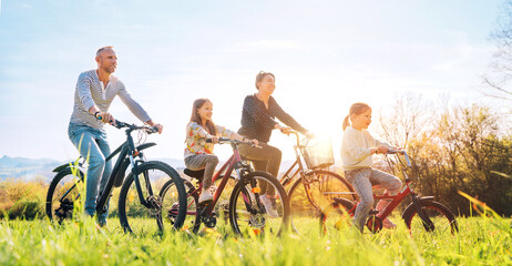 Smiling father and mother with two daughters during summer outdoor bicycle riding. They enjoy...