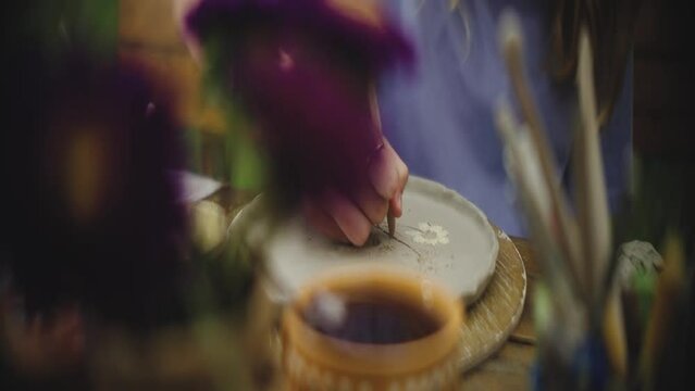 Selective-focus view of a person curving designs on a clay plate
