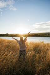 Relaxed woman enjoying fresh air at windy lake during autumn sunset. Freedom and happiness outdoors