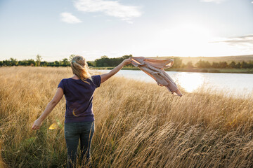 Woman standing in grass and enjoying windy weather at lake during autumn sunset