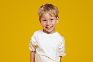 Happy little blonde male kid boy in white tshirt laughing at camera against orange background - obrazy, fototapety, plakaty