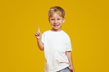 Handsome shy little boy wearing white t-shirt, smiling and pointing up while looking away