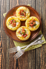 Baked mashed potato nests with bacon closeup on the plate on the wooden table. Vertical top view from above