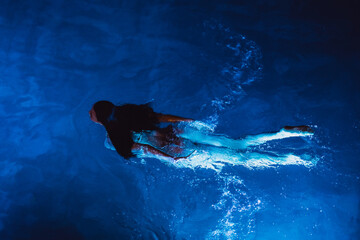 Calm beautiful young woman relaxing in a swimming pool at night, view from above. High-quality photo