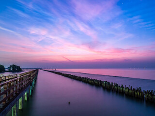 Fototapeta na wymiar Sea view near mangrove forest with man made wooden barrier for wave protection, under morning twilight colorful sky in Bangkok, Thailand