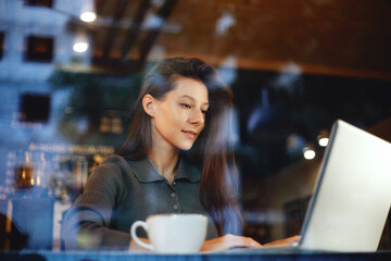 Portrait of young cute brunette woman using laptop computer at a cafe