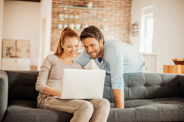 Young couple using a laptop on the couch in the living room at home