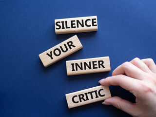Silence your inner critic symbol. Wooden blocks with words Silence your inner critic. Beautiful deep blue background. Businessman hand. Business and Silence your inner critic concept. Copy space.