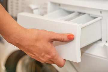 A woman opens the tray for pouring laundry detergent into the washing machine. The concept of...