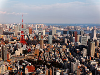 An aerial panorama from Roppongi over Downtown Tokyo, with landmark Tokyo Tower among crowded buildings, city streets crisscrossing the district & Tokyo Bay on distant horizon on a beautiful sunny day